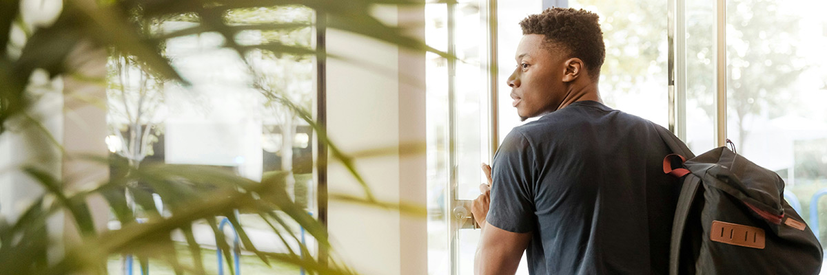 student with backpack in front of an office glass door